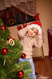 快乐的小男孩穿着米色毛衣和圣诞老人的帽子站在窗前图片
