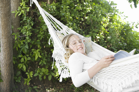 女孩躺在一张吊床在花园里读一本书微笑高清图片