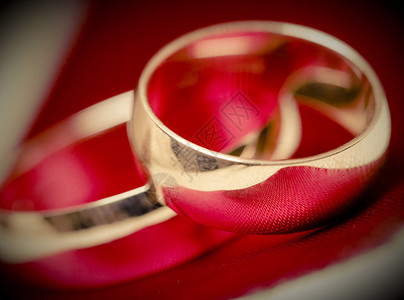 红色背景下结婚金戒指的特写图片