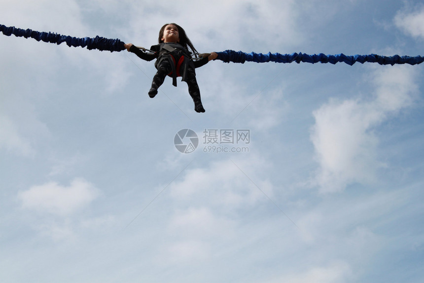 小女孩在蓝天背景的蹦极上跳跃图片