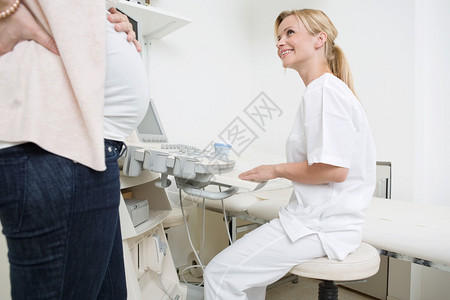 在诊所看孕妇时使用超声波机的年轻女医生图片