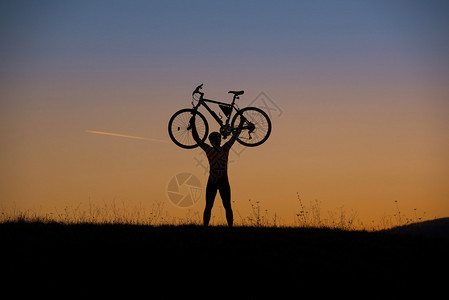 山上骑脚踏车的休修会在日落时在草地图片
