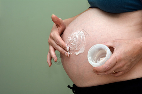 孕妇在她的腹部涂抹美容润肤霜怀孕妇家庭父母身份母亲身份的概念照图片