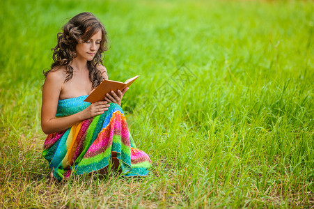 年轻漂亮的黑发卷美女的肖像在夏日绿色公园拿着书图片