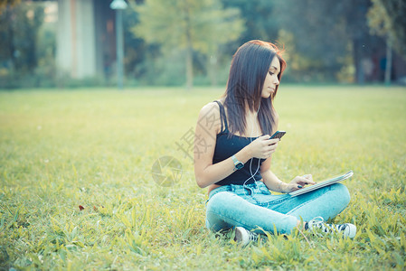 坐在户外草地上使用平板和智能手机的白图片