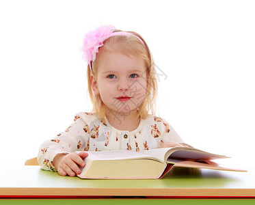 头戴弓的金发小女孩坐在办公桌前读一本厚书图片