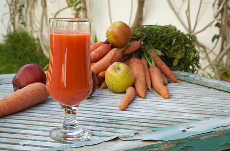 一杯新鲜的苹果胡萝卜汁在木质表面上背景中的新鲜胡萝卜和苹果复图片