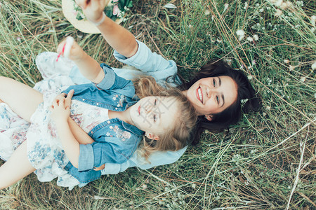 年轻母亲和有糖果的女儿在绿草背图片