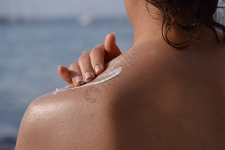 年轻女子在海滩上的肩膀上涂防晒霜图片