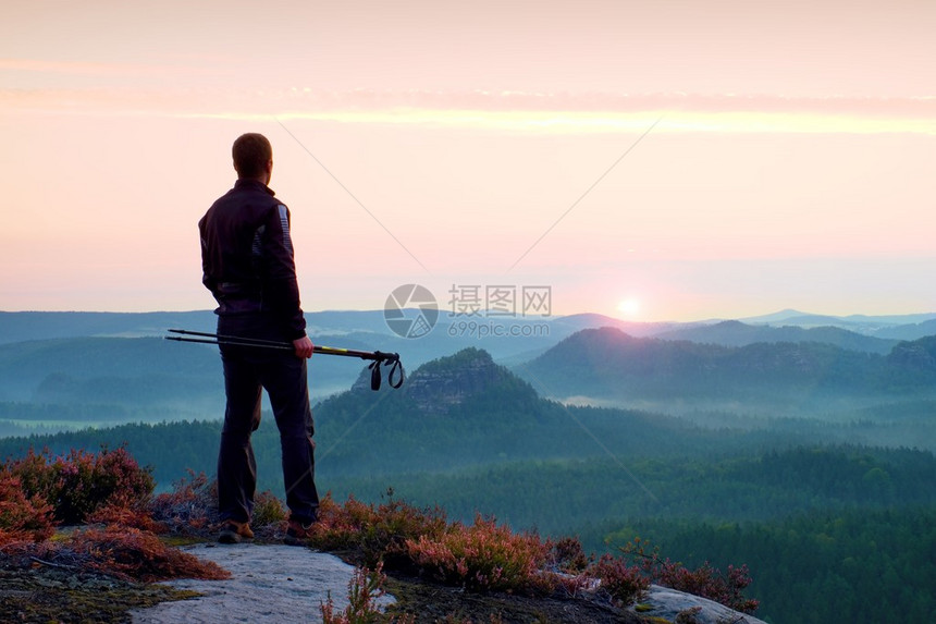 手拿着杆的导游的剪影穿着运动服的徒步旅行者站在迷雾笼罩的山谷上空阳光明媚的春天破图片