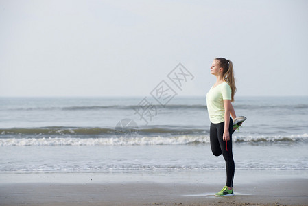 一个运动的年轻女子在沙滩上伸展运动的图片