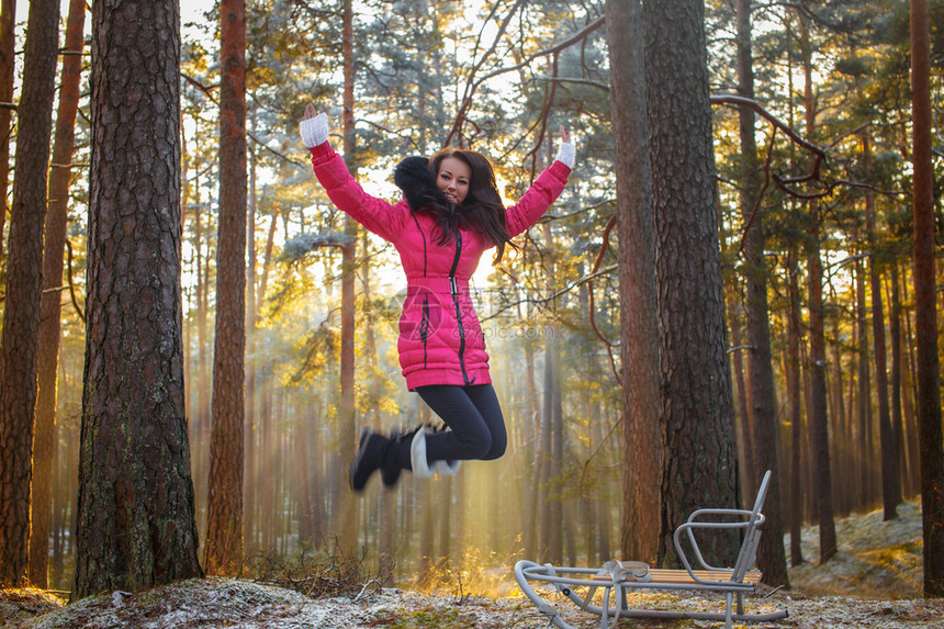 穿粉红色大衣的女孩在冬季森林里跳跃背景图片