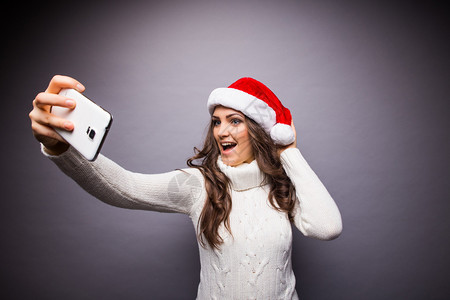 美丽的女孩的圣诞肖像戴着圣诞老人帽子的女孩女孩在手机图片