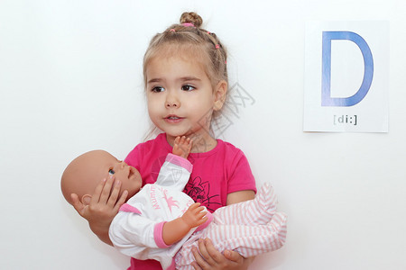 可爱的小女孩拥抱一个洋娃唱着摇篮曲在白色背景和D字母上背景图片