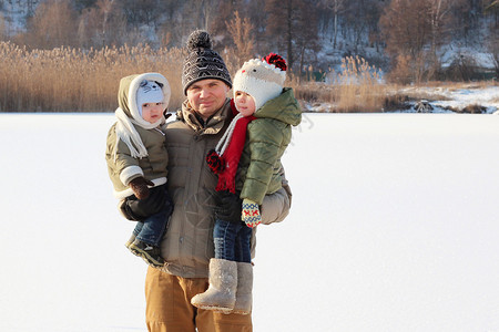 和两个小孩玩乐的快乐男人在寒冷湖岸边过冬日图片