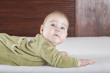 六个月大的金发碧眼婴儿绿色天鹅绒连体衣躺在白色床单上图片