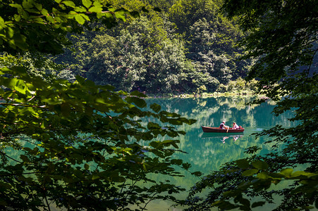 两个人的小木船树木框架中的森林湖Biogradska山公园黑山的背景图片