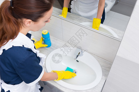 对持黄色橡胶手套蓝海绵和洗涤粉清洗槽的女管家图片