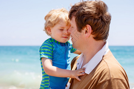 父亲和蹒跚学步的小男孩在海洋滩上的画像男人和孩子儿拥抱无忧虑的童年图片