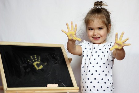可爱的小女孩在黑板上用粉笔手掌画着她图片