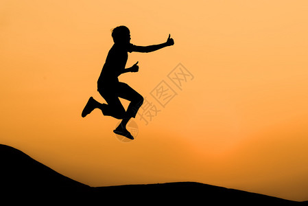 男人在欢快的跳跃中在橙色日落天背景图片
