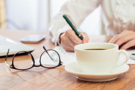 在书桌上写作和喝咖啡的女商图片
