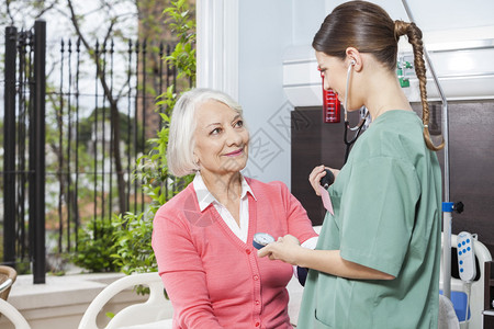 在康复中心检查微笑老年患者血压的女护士图片