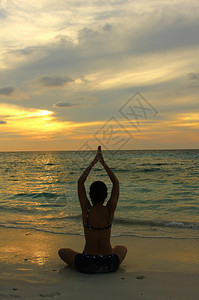 日落时在沙滩上练习瑜伽的年轻女子剪影图片