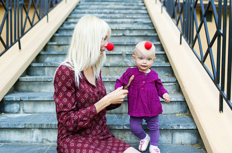 母亲和有小丑鼻子的小女儿坐着梯子坐图片