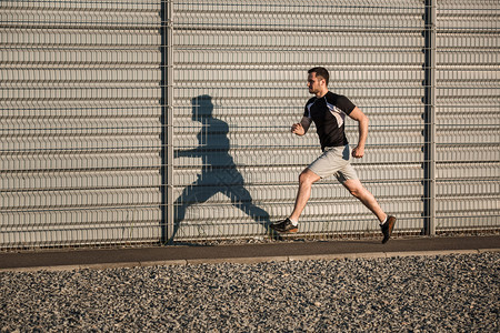 健壮的男子在户外沿着美丽的灰色墙壁奔跑的全长肖像图片