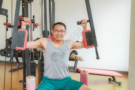 亚洲中年男子在健身房训练手臂设备以图片