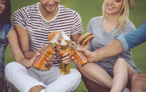 时尚朋友在公园休息时碰杯饮料吃三明治和微图片