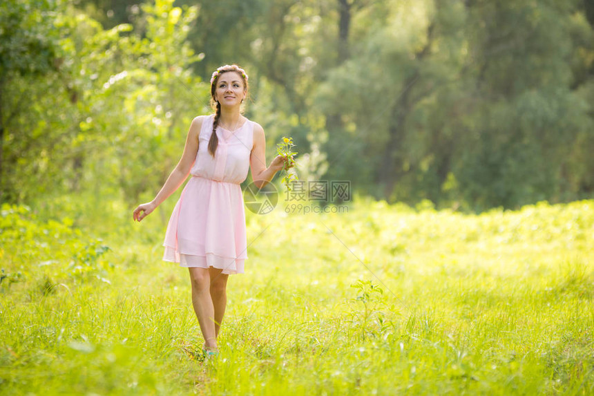 年轻美丽的女士在绿色草地上行走带着一束花朵穿图片