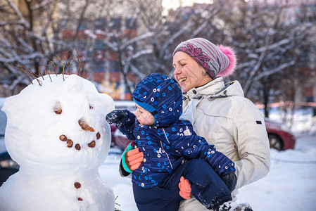 小孩男在美丽的冬日让雪人户外做雪人图片