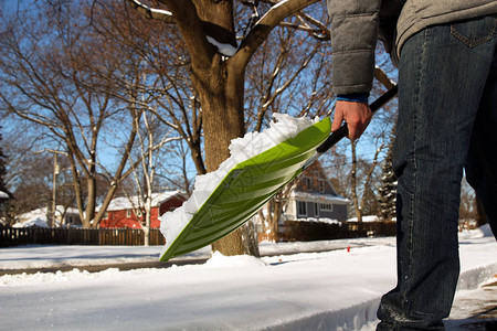 男子在郊区自家门前铲雪背景图片