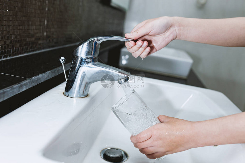 女人从不锈钢或镀铬水龙头或水龙头里装满一杯水图片