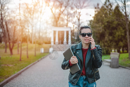 年轻妇女使用智能电话在公园用笔记本电脑行走时手图片
