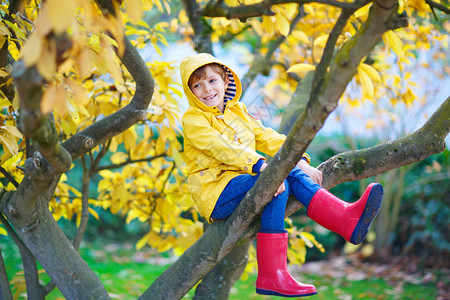 学龄前儿童穿着黄色雨衣和红色橡胶靴学习攀爬图片