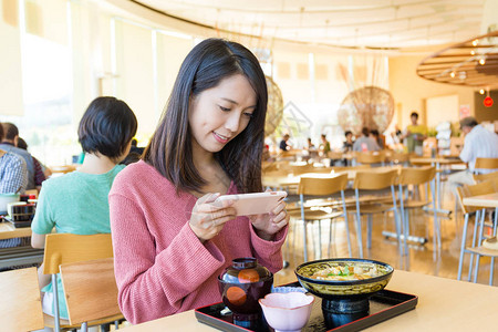 女人在餐厅的食物上用手机照相图片