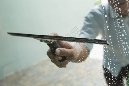 使用刮刀清洗窗户的玻璃清洁剂图片