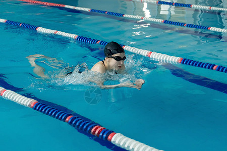 年轻女子在护目镜和帽在蓝色的水室内比赛池游泳蛙泳描边样式背景图片