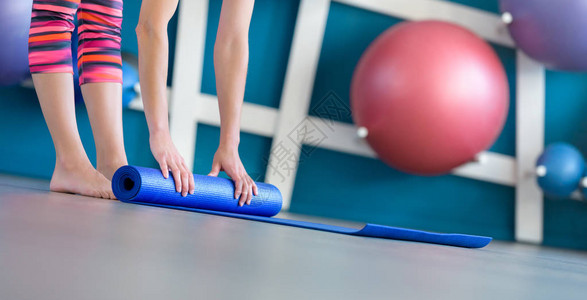 年轻女在锻炼后折叠蓝瑜伽或健身垫子图片