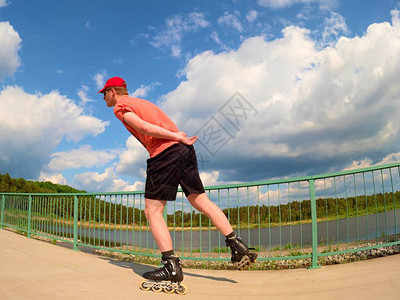 短筒靴身穿红色t恤和黑色裤子的直排轮滑运动员在桥上滑冰的后视图在湖桥上光滑的混凝土地面上进行户外直排轮滑穿四轮靴背景
