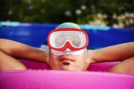一个戴着潜水面罩浴帽和亮粉色游泳圈的白人年轻男子的特写图片