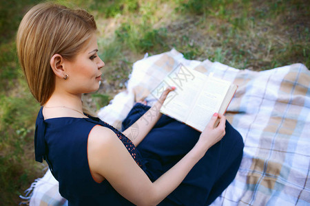 穿着深蓝色裙子的金发女孩坐在格子上阅读这本书假期节日图片