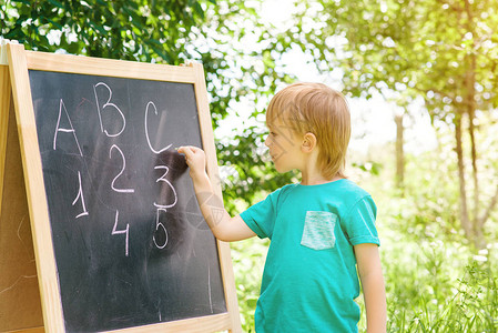 可爱的小男孩在花园的黑板上写信和数字图片