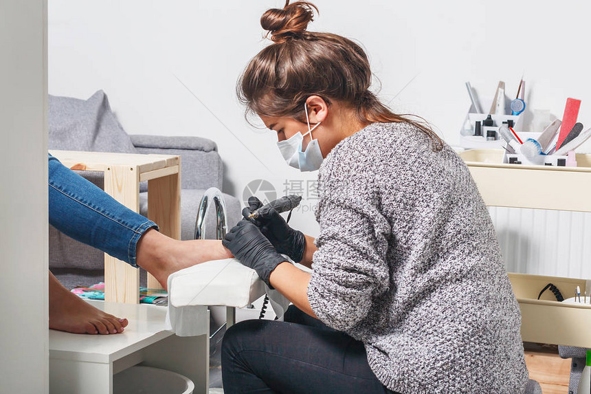 一个年轻的白人美甲师女孩在工作场所为客户制作修脚电动指甲钻机图片