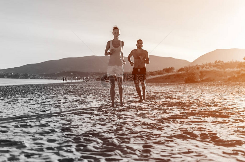 快乐的一对年轻夫妇在沙滩上光着脚跑来去图片