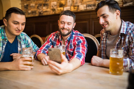 快乐的老朋友在酒吧里玩智能手机喝着啤酒图片