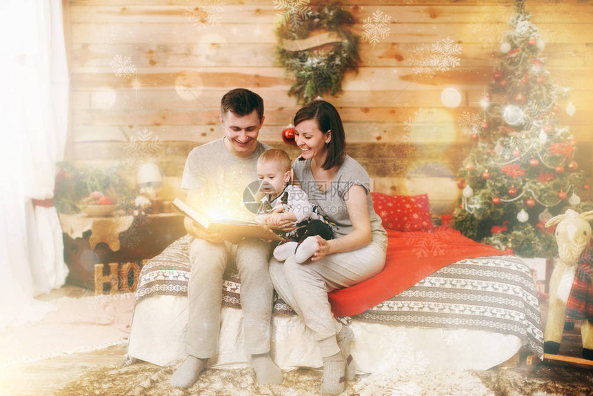 年轻快乐的父母带着小孩的儿子在家里装饰圣诞树附近的新年木屋里读童话故事生活方式家庭和假日2018概念神图片